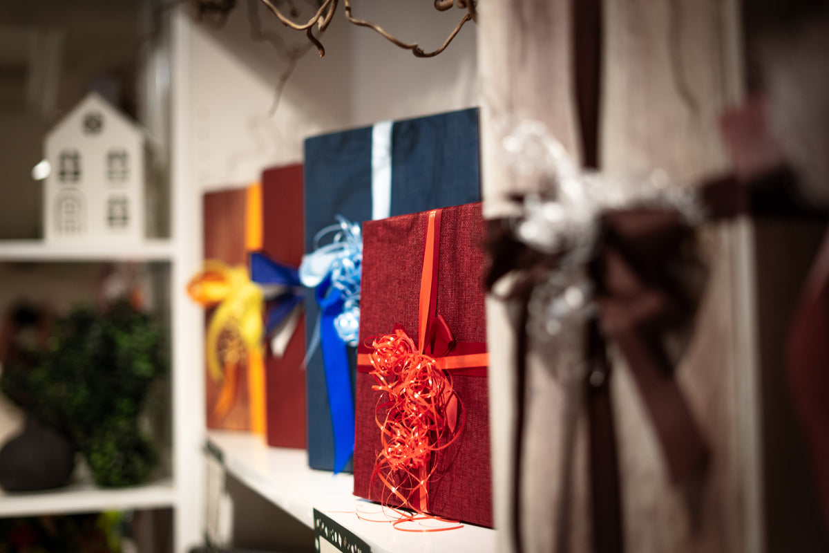 Mehrere dekorative Geschenkboxen in kräftigen Farben wie Dunkelrot und Blau, verziert mit farblich passenden Schleifen, aufgereiht auf einem Regal.