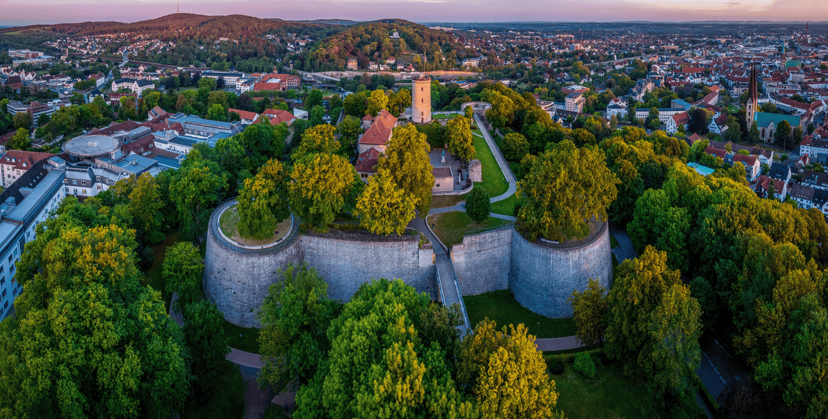 Panoramablick auf die Sparrenburg in Bielefeld, umgeben von üppigem Grün und Stadtlandschaft.