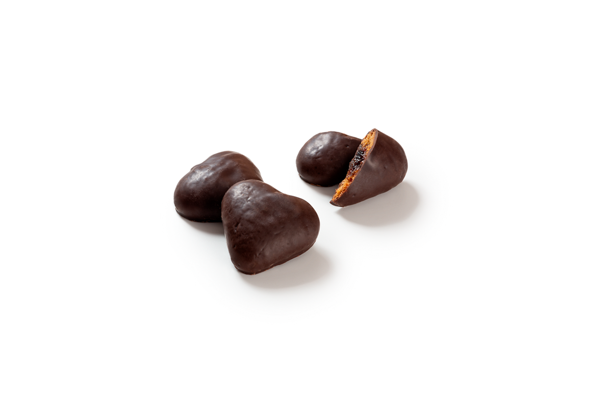 Produktaufnahme von herzförmigen Lebkuchen, vollständig mit dunkler Schokolade überzogen. Ein Lebkuchenherz ist halbiert und offenbart die saftige, dunkle Kirschfruchtfüllung im Inneren.