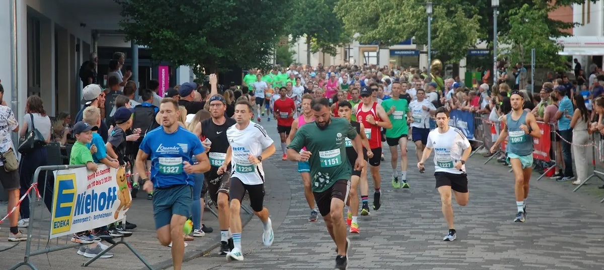 Läuferinnen und Läufer mit Startnummern beim Citylauf „Die Nacht von Borgholzhausen“ auf einer belebten Straße, angefeuert von zahlreichen Zuschauern am Rand.