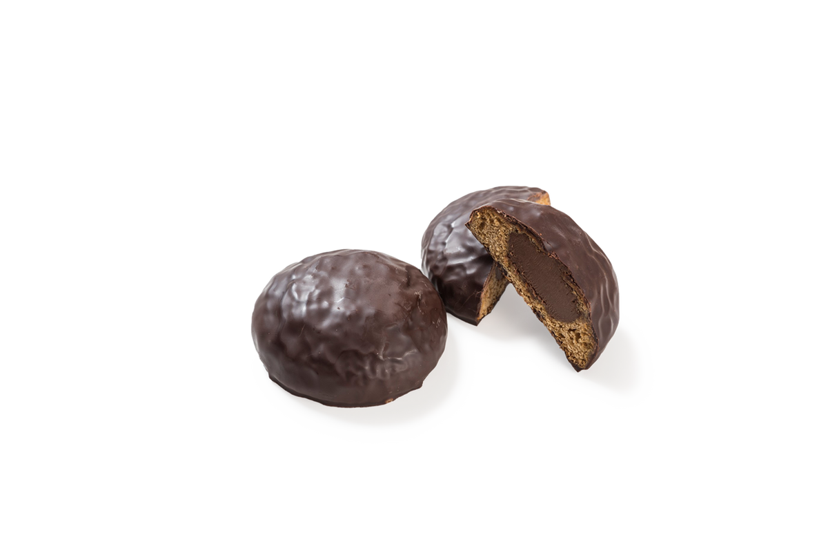 Produktaufnahme von runden Lebkuchen-Spezialitäten, sogenannten Nougat-Bomben. Ein Stück liegt als Ganzes vor, während ein weiteres halbiert ist und den Blick auf die cremige Nougatfüllung im Inneren sowie den feinporigen Lebkuchenteig freigibt. Alle Stücke sind mit einer glänzenden Schicht dunkler Schokolade überzogen.