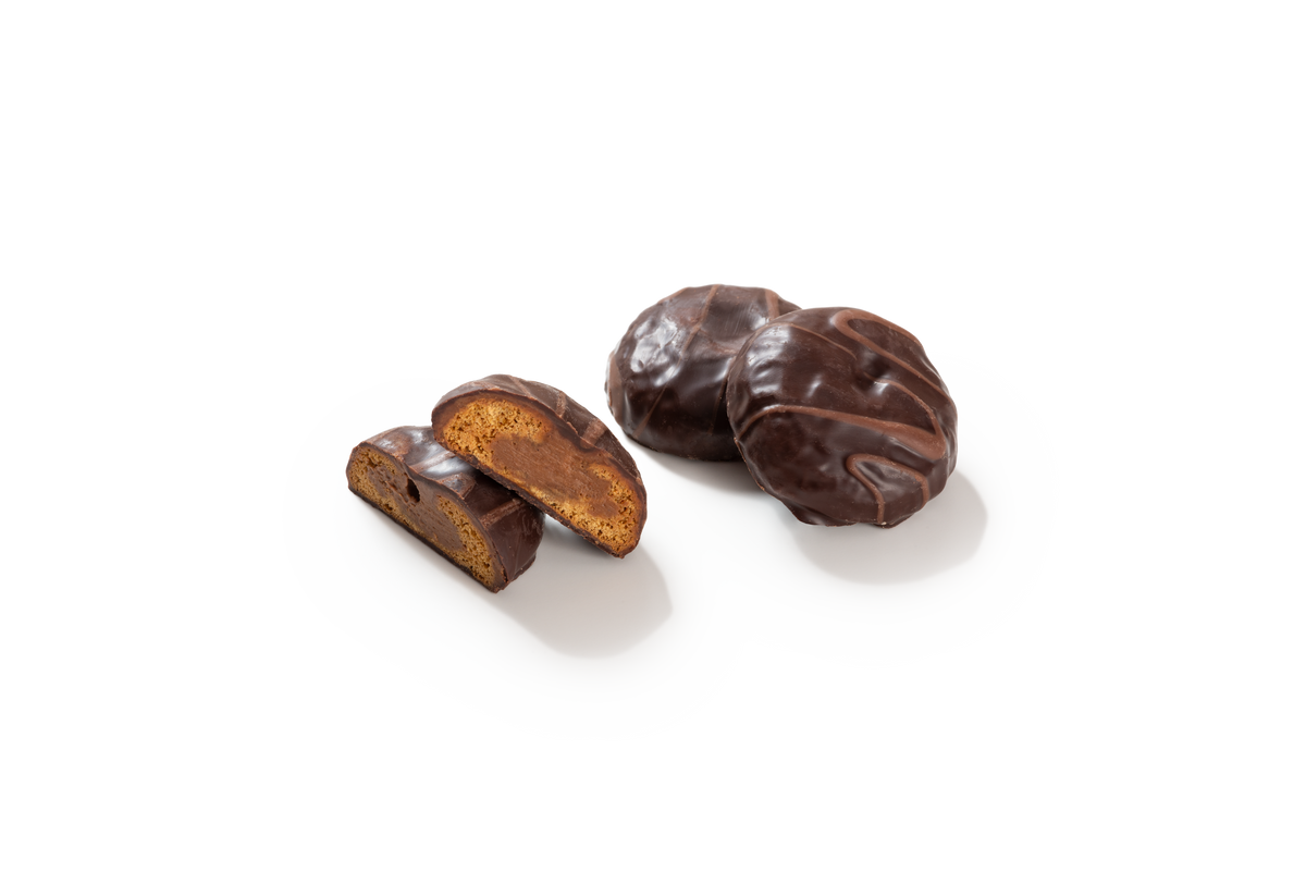 Produktaufnahme von runden Nougat-Talern. Zwei der Lebkuchen-Spezialitäten liegen als Ganzes vor und sind mit einem feinen Schokoladenmuster verziert, während zwei weitere halbiert sind und den Blick auf den feinporigen Lebkuchenteig sowie die cremige Nougatfüllung im Inneren freigeben. Alle Stücke sind mit dunkler Schokolade überzogen.