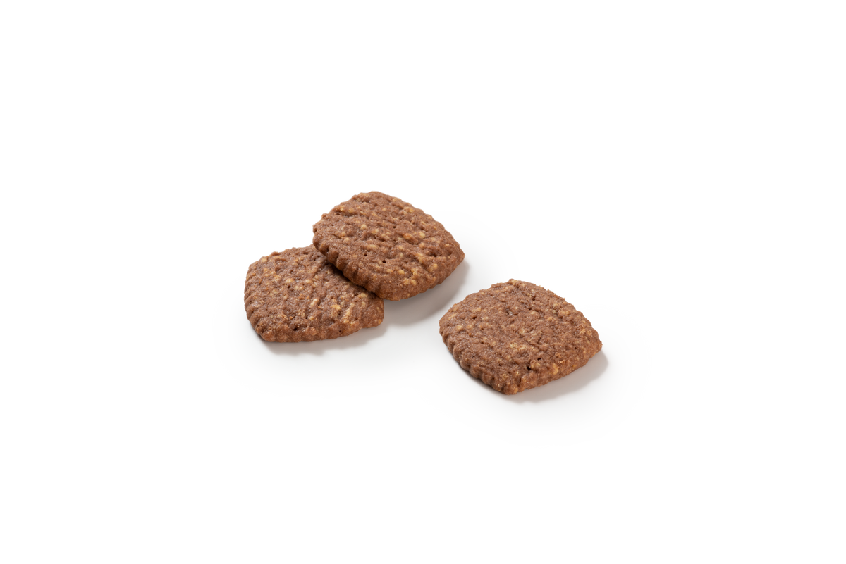 Produktaufnahme von drei Piumer Schokini Mürbegebäck-Stücken. Die quadratischen Kekse mit abgerundeten Ecken sind dunkelbraun und mit deutlich sichtbaren, hellen weißen Schokoraspeln durchzogen. 
