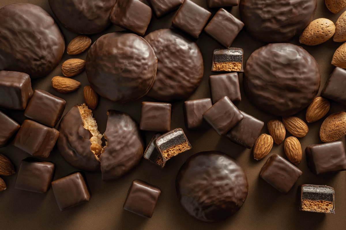 Verschiedene Lebkuchen sowie Dominosteine und Mandeln drapiert auf einem braunem Hintergrund. Von oben fotografiert.
