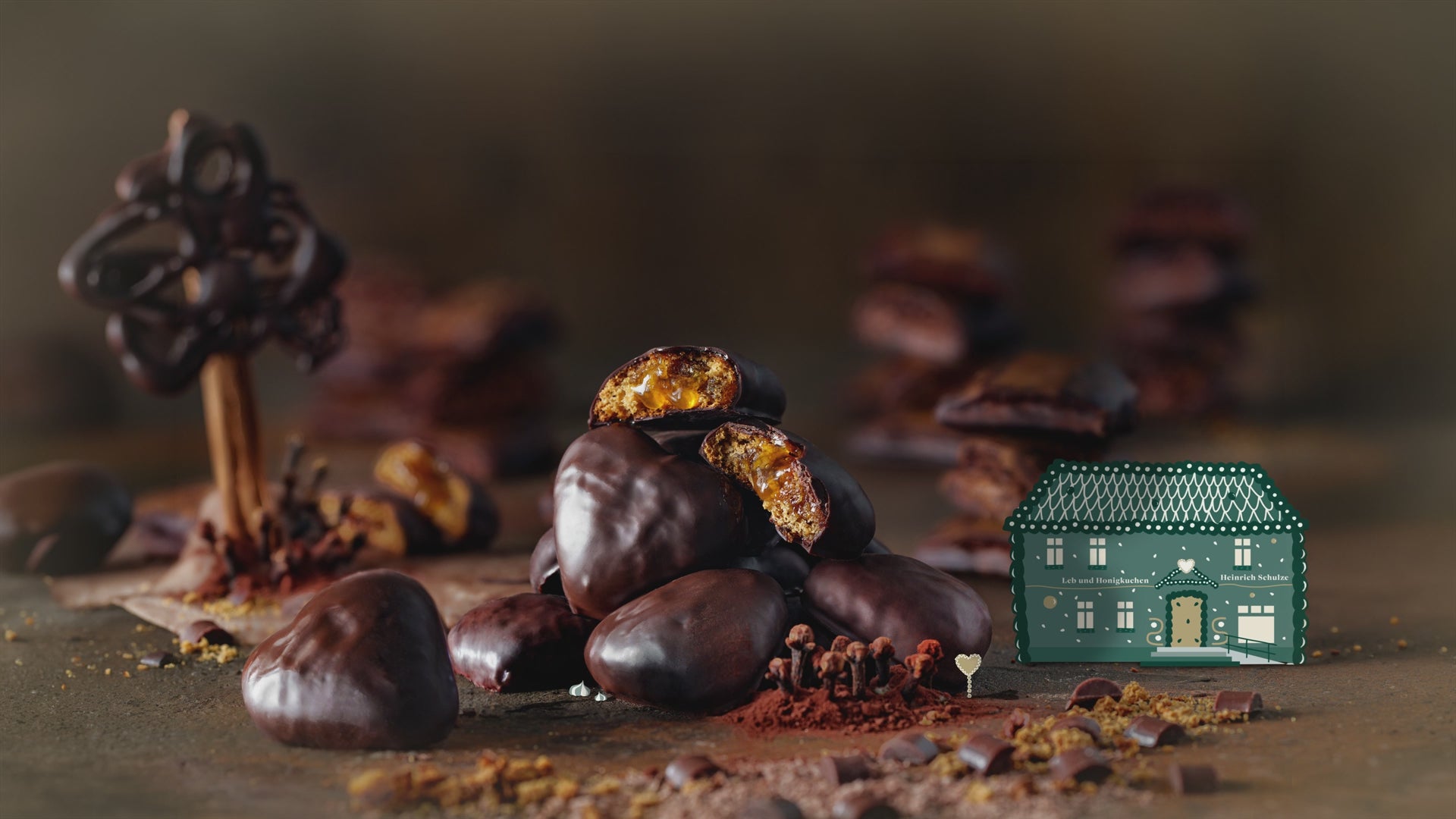 Berg aus gefülltem, mit Schokolade überzogenem Lebkuchen und eine Illustration des Stammhauses und Menschen, die sich zwischen den Lebkuchen bewegen. 